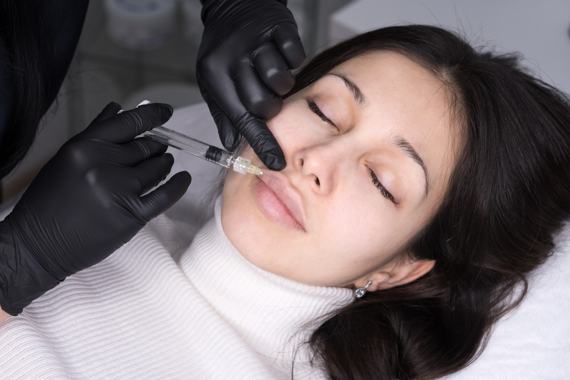 A practitioner preparing to administer lip filler to a patient in a stylish clinic setting, with syringes