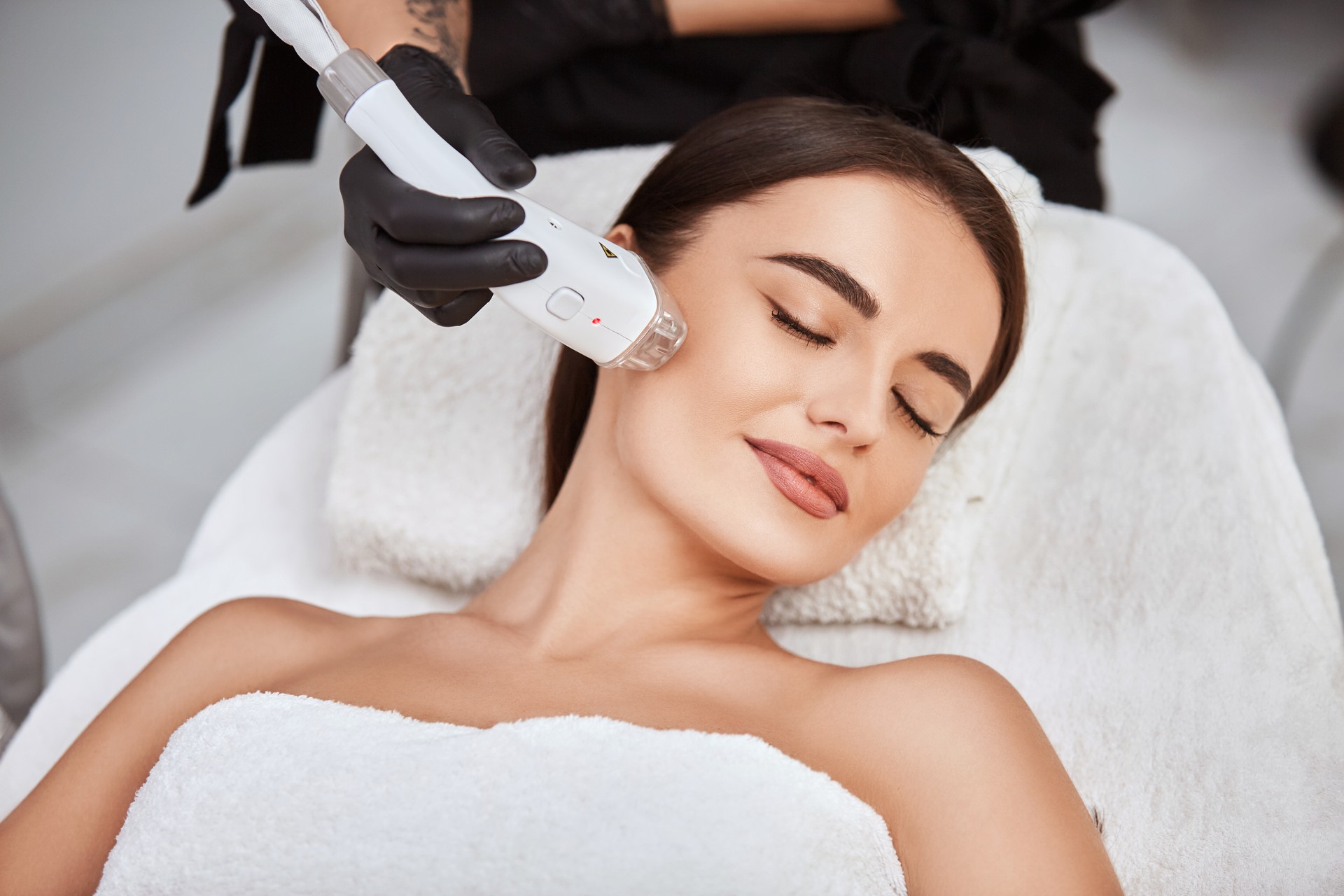 A clinician administering laser skin treatment to a patient in a bright, well-equipped clinic, with laser equipment